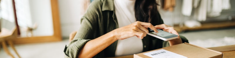 Young woman using mobile device to scan package using shipping software with delivery and shipping notifications on mobile device