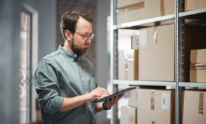 How Desktop Shipping Software with Rate Shopping is Improving Business Shipping and Logistics featuring man in mail center scanning packages on ipad